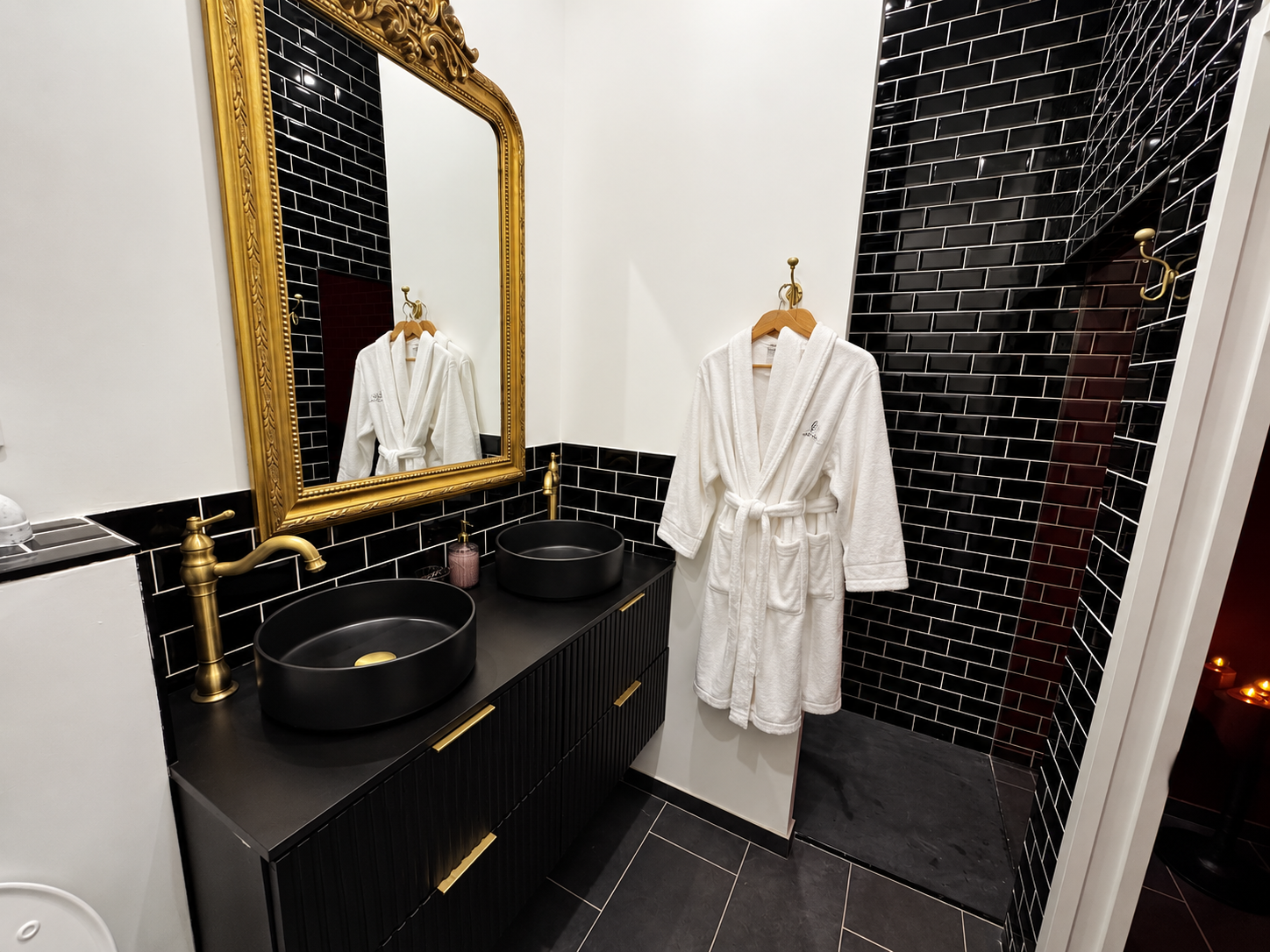 Salle de bain avec double vasque noire, miroir doré et douche.